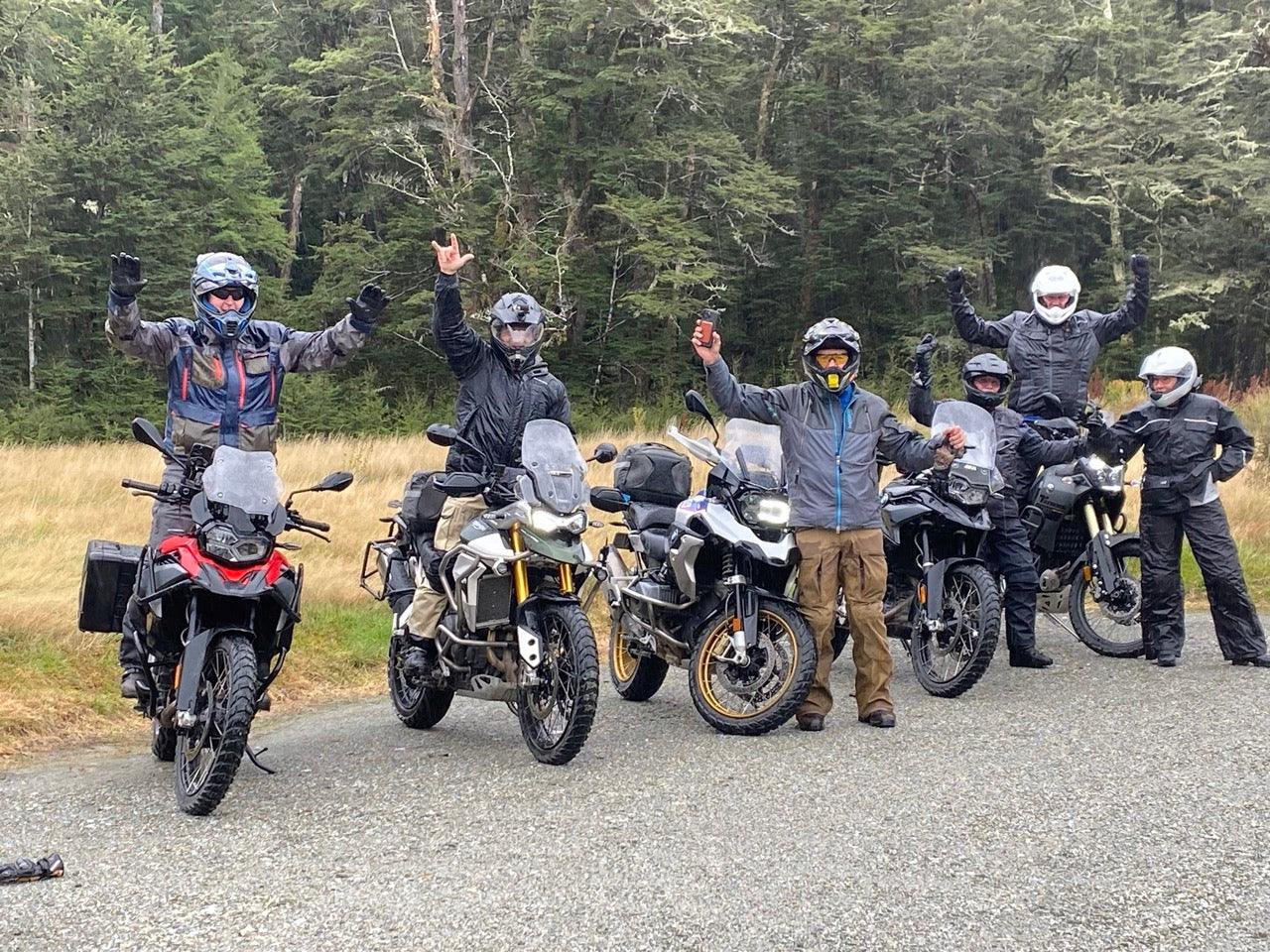A group of joyful motorcyclists raising their arms in celebration on a forest-lined road