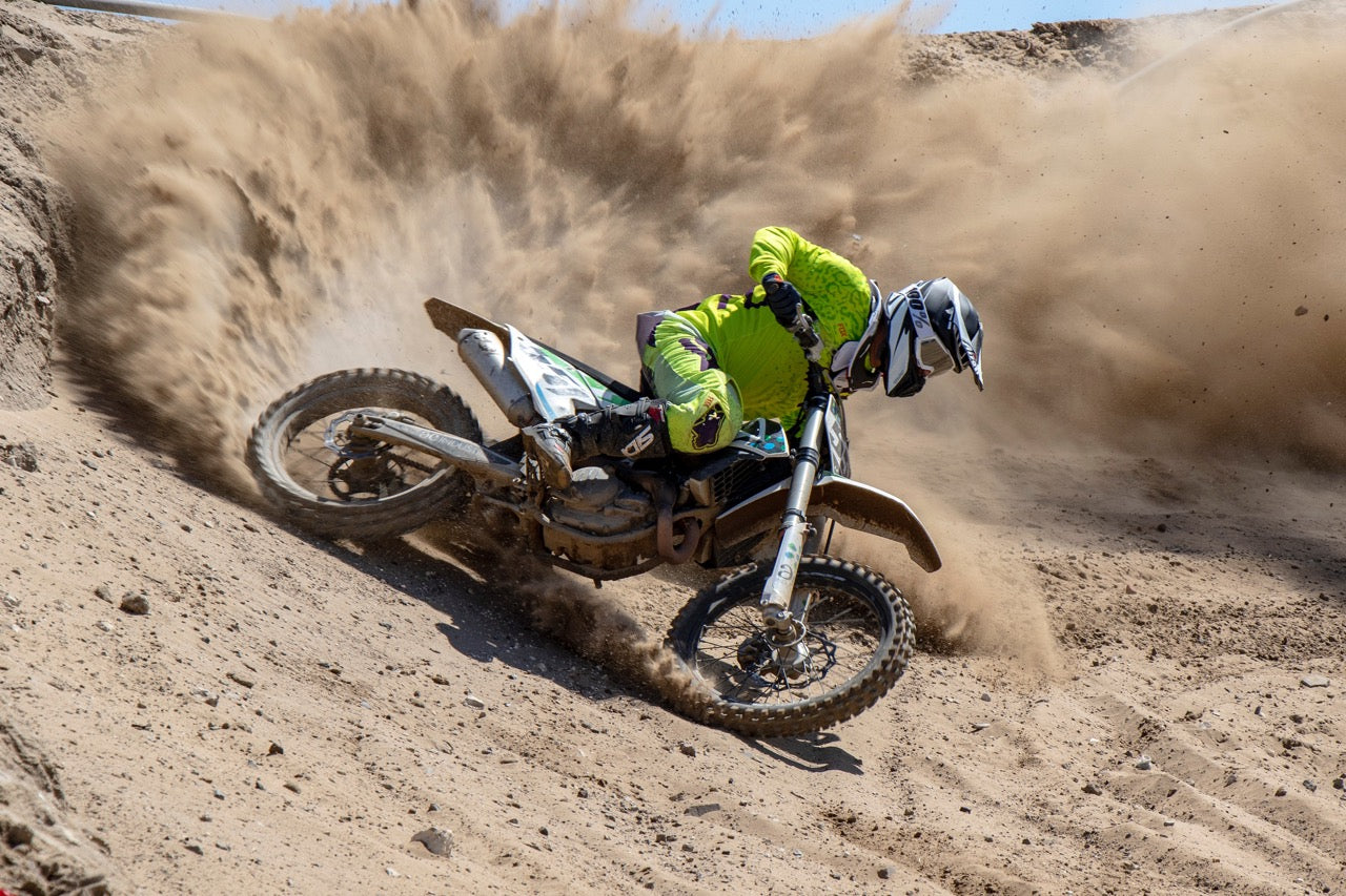 Male motocross rider racing in dust rear view